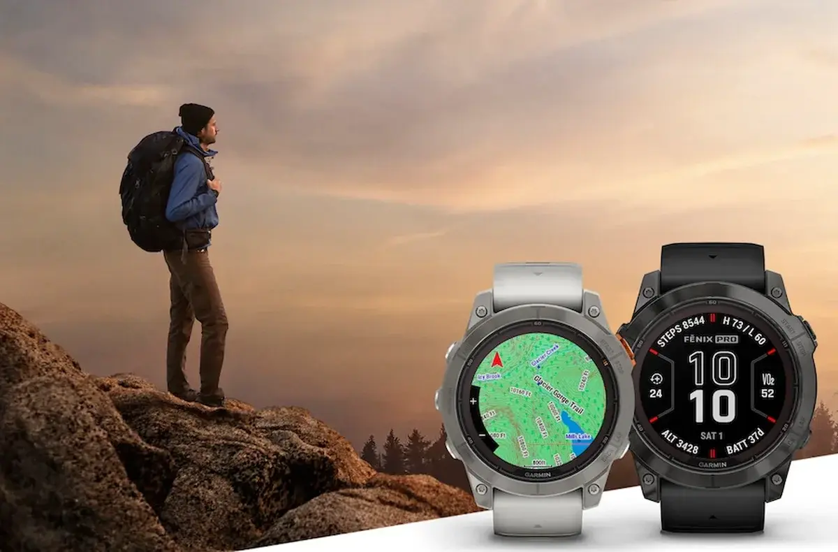 Montañero en cumbre al atardecer con dos relojes Garmin Fénix en primer plano mostrando mapa topográfico y pantalla MIP