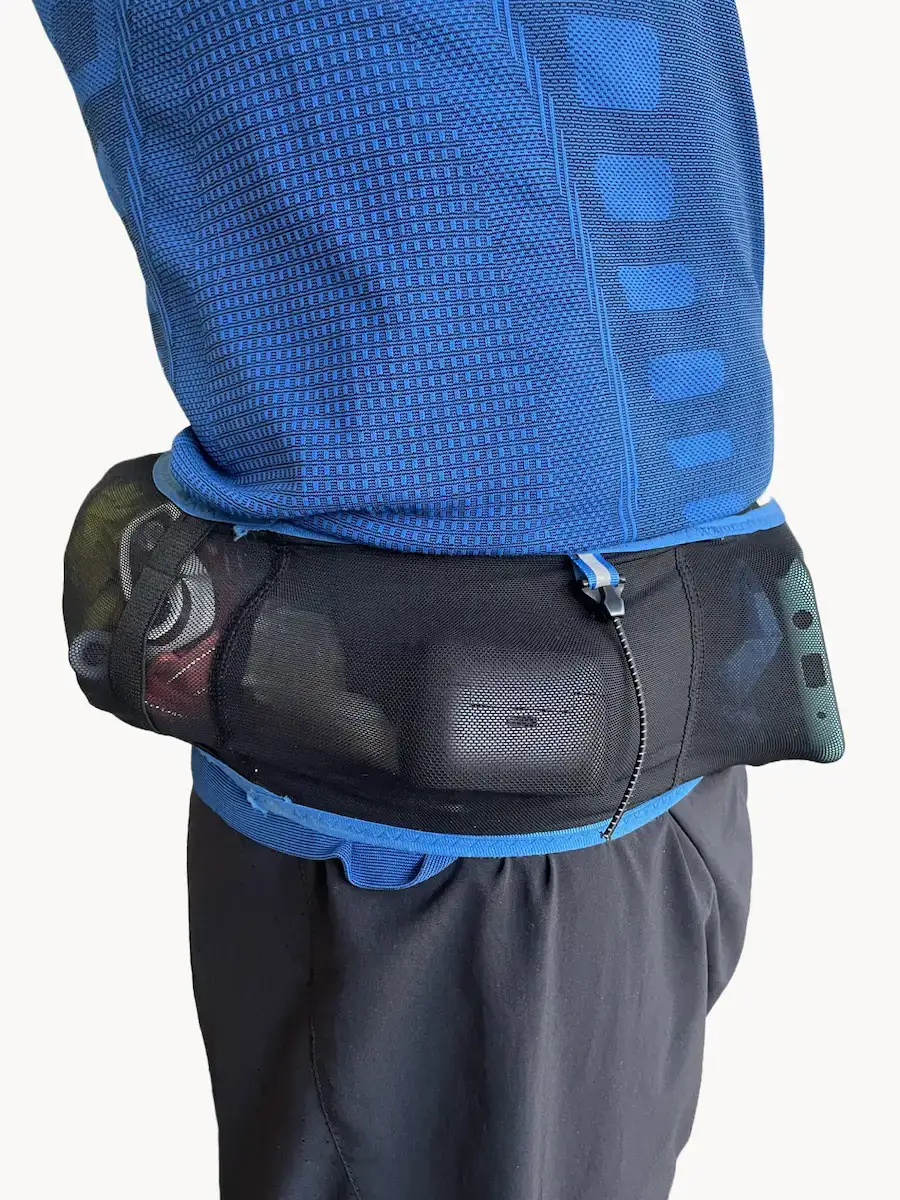 AONIJIE PRO puesto y cargado, vista lateral mostrando el bolsillo trasero con soft flask y cortavientos